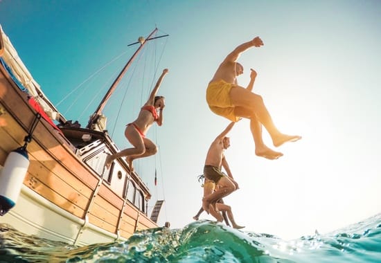 Young adults jumping from a yacht into the ocean