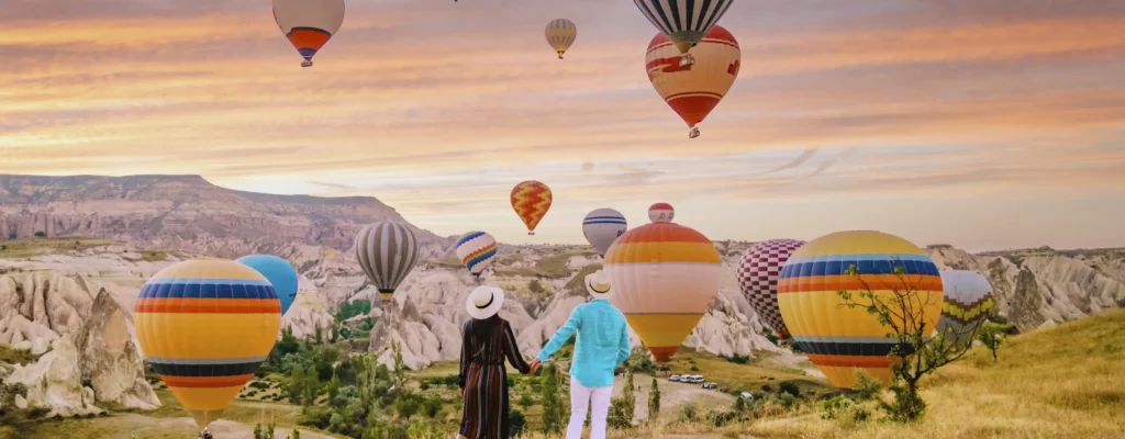 Couple holding hands while watching a group of colourful hot air balloons